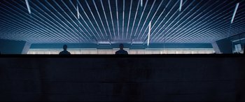 Movie still from “No Time to Die” (2021), directed by Cary Joji Fukunaga – A person sitting in a room with a fence; Extreme Wide shot, Low angle