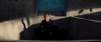 Movie still from “No Time to Die” (2021), directed by Cary Joji Fukunaga – A man sitting on a ledge in the sunlight; Medium shot, High angle