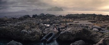 Movie still from “No Time to Die” (2021), directed by Cary Joji Fukunaga – Two people standing on a rocky shore near an inflatable boat; Extreme Wide shot, High angle