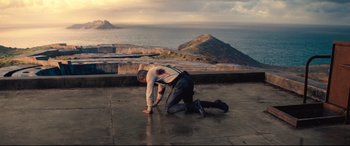 Movie still from “No Time to Die” (2021), directed by Cary Joji Fukunaga – A man kneeling down on the ground near the ocean; Wide shot, High angle