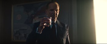 Movie still from “No Time to Die” (2021), directed by Cary Joji Fukunaga – A man in a suit and tie holding a glass of wine; Medium shot, Low angle