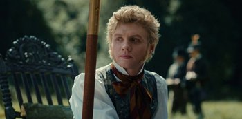 Movie still from “The Empress” (2022), created by Katharina Eyssen – A man in a vest and tie holding a wooden stick; Close Up shot, Over the shoulder angle