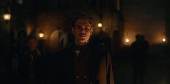 Movie still from “The Empress” (2022), created by Katharina Eyssen – A man in a suit and tie standing in the dark; Medium shot, Low angle
