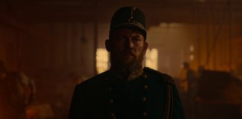 Movie still from “The Empress” (2022), created by Katharina Eyssen – A man wearing a uniform and a hat is standing in a room; Medium shot, Low angle