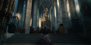 Movie still from “The Empress” (2022), created by Katharina Eyssen – A woman in a dress sitting in front of an altar; Extreme Wide shot, Low angle