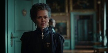 Movie still from “The Empress” (2022), created by Katharina Eyssen – A woman in a black jacket with a cross on her chest; Close Up shot, Over the shoulder angle