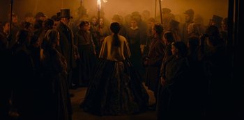 Movie still from “The Empress” (2022), created by Katharina Eyssen – A group of people gathered around a woman in a long dress; Wide shot, Over the shoulder angle