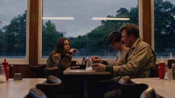 Movie still from “The End of the F***ing World” (2017), directed by Jonathan Entwistle – A group of people sitting at a table in front of a window; Medium shot, Over the shoulder angle