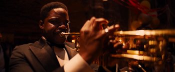 Movie still from “Babylon” (2022), directed by Damien Chazelle – A man in a suit smoking a cigarette while holding a trumpet; Close Up shot, Low angle