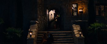 Movie still from “Babylon” (2022), directed by Damien Chazelle – Two people sitting on the steps in front of a doorway; Wide shot, High angle
