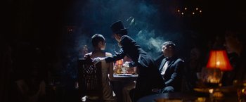 Movie still from “Babylon” (2022), directed by Damien Chazelle – A group of people sitting around a table; Wide shot, Over the shoulder angle
