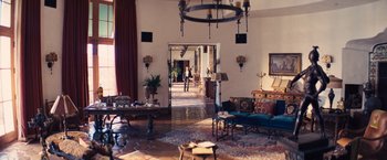 Movie still from “Babylon” (2022), directed by Damien Chazelle – A living room filled with lots of furniture and potted plants; Extreme Wide shot, High angle