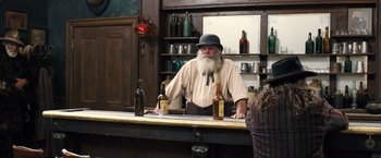 Movie still from “Babylon” (2022), directed by Damien Chazelle – An old man standing at a bar with two bottles of beer; Medium shot, Over the shoulder angle