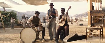 Movie still from “Babylon” (2022), directed by Damien Chazelle – A group of men playing musical instruments on a beach; Wide shot, Low angle