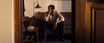 Movie still from “Babylon” (2022), directed by Damien Chazelle – A man sitting on top of a wooden bench in front of a lamp; Medium shot, High angle