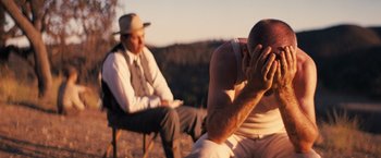 Movie still from “Babylon” (2022), directed by Damien Chazelle – Two men sitting on a chair and one is holding his hands to his face; Medium shot, Low angle