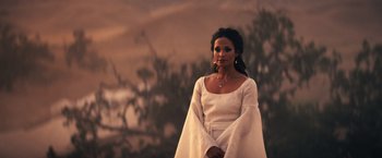 Movie still from “Babylon” (2022), directed by Damien Chazelle – A woman in a white dress standing in front of trees; Medium shot, Over the shoulder angle