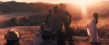 Movie still from “Babylon” (2022), directed by Damien Chazelle – A group of people standing on top of a grass covered field; Wide shot, Over the shoulder angle