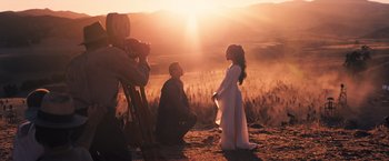 Movie still from “Babylon” (2022), directed by Damien Chazelle – A man kneeling down next to a little girl in a field; Wide shot, Over the shoulder angle