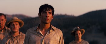 Movie still from “Babylon” (2022), directed by Damien Chazelle – A man in a tan shirt is standing in front of a forest; Close Up shot, Low angle
