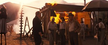 Movie still from “Babylon” (2022), directed by Damien Chazelle – A group of men standing next to each other near a fire; Wide shot, Over the shoulder angle