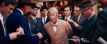 Movie still from “Babylon” (2022), directed by Damien Chazelle – A group of men standing next to each other in a crowd; Medium shot, Over the shoulder angle