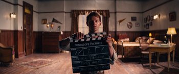 Movie still from “Babylon” (2022), directed by Damien Chazelle – A man is holding a clapperboard in a room; Medium shot, Low angle