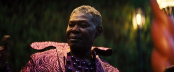 Movie still from “Babylon” (2022), directed by Damien Chazelle – An older man wearing a purple jacket and a purple bead necklace; Close Up shot, Low angle
