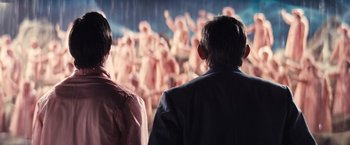 Movie still from “Babylon” (2022), directed by Damien Chazelle – Two people watching a crowd of people in the rain; Medium shot, Over the shoulder angle