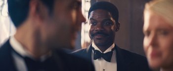 Movie still from “Babylon” (2022), directed by Damien Chazelle – A man wearing a tuxedo and a black bow tie; Close Up shot, Over the shoulder angle