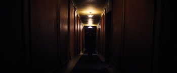 Movie still from “Babylon” (2022), directed by Damien Chazelle – A person standing in a dark hallway with lights on; Wide shot, Low angle