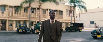 Movie still from “Babylon” (2022), directed by Damien Chazelle – A man in a suit and tie standing in a parking lot; Medium shot, Over the shoulder angle
