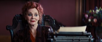 Movie still from “Babylon” (2022), directed by Damien Chazelle – An older woman sitting in a chair in front of a stack of books; Close Up shot, Low angle