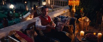 Movie still from “Babylon” (2022), directed by Damien Chazelle – A man sitting on top of a couch holding a drink; Medium shot, High angle