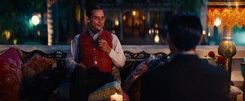 Movie still from “Babylon” (2022), directed by Damien Chazelle – A man sitting on top of a couch next to a candle; Medium shot, Over the shoulder angle