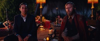 Movie still from “Babylon” (2022), directed by Damien Chazelle – A man sitting at a table in front of candles; Medium shot, Over the shoulder angle