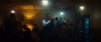 Movie still from “Babylon” (2022), directed by Damien Chazelle – A group of men playing musical instruments in a room; Extreme Wide shot, Low angle