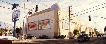 Movie still from “Babylon” (2022), directed by Damien Chazelle – Cars parked on the side of the street near a building; Extreme Wide shot, Low angle