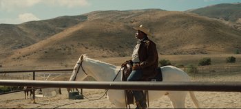 Movie still from “Nope” (2022), directed by Jordan Peele – A man sitting on top of a white horse in the desert; Wide shot, Over the shoulder angle