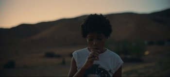 Movie still from “Nope” (2022), directed by Jordan Peele – A woman is eating something while standing in a field; Medium shot, Low angle