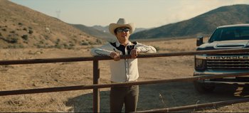 Movie still from “Nope” (2022), directed by Jordan Peele – A man in a cowboy hat leaning on a fence; Medium shot, Over the shoulder angle