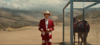 Movie still from “Nope” (2022), directed by Jordan Peele – A man in a suit and cowboy hat standing in the desert; Wide shot, Over the shoulder angle