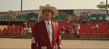 Movie still from “Nope” (2022), directed by Jordan Peele – A man in a red suit and white cowboy hat stands in front of an audience; Medium shot, Over the shoulder angle