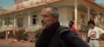 Movie still from “Nope” (2022), directed by Jordan Peele – An older man wearing a black shirt and a black scarf; Close Up shot, Low angle