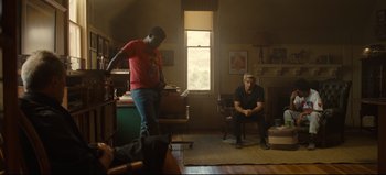 Movie still from “Nope” (2022), directed by Jordan Peele – Two men sitting in a living room and one is holding a book; Wide shot, Over the shoulder angle