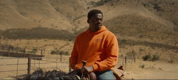 Movie still from “Nope” (2022), directed by Jordan Peele – A man in an orange hoodie riding on a horse; Medium shot, Over the shoulder angle