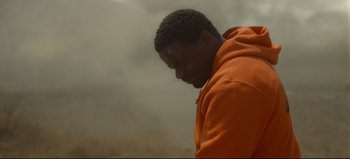 Movie still from “Nope” (2022), directed by Jordan Peele – A man in an orange hoodie is looking down; Close Up shot, High angle