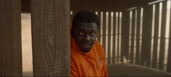 Movie still from “Nope” (2022), directed by Jordan Peele – A man in an orange hoodie leaning against a wooden pole; Close Up shot, High angle
