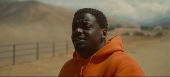 Movie still from “Nope” (2022), directed by Jordan Peele – A man in an orange hooded sweatshirt standing on a dirt road; Close Up shot, Over the shoulder angle