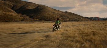 Movie still from “Nope” (2022), directed by Jordan Peele – A man riding a motorcycle on a dirt road; Extreme Wide shot, High angle